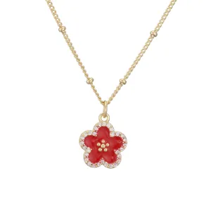 Detaillierte Nahaufnahme einer vergoldeten Kette mit rotem Emaille-Blumenanhänger und Kristallen