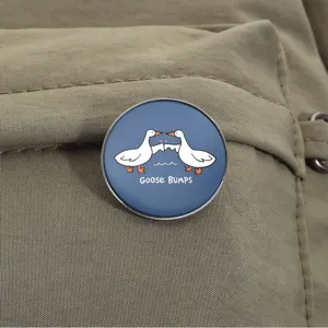 Funny round metal brooch featuring white geese bumping wings on a khaki backpack