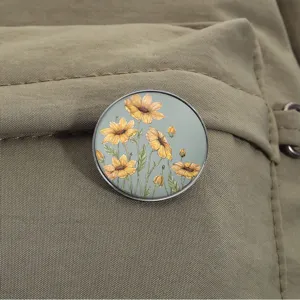 Vintage round metal brooch featuring painted sunflower botanical design on a backpack