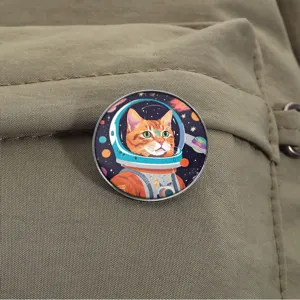 Round metal enamel pin badge featuring a cute ginger tabby cat astronaut in space