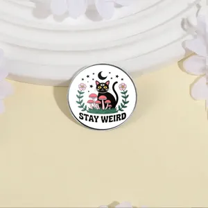 Simpatica spilla tonda in smalto con gatto nero, funghi e scritta Stay Weird design