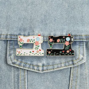 Close-up of vintage floral sewing machine enamel pins in black and white on denim jacket.
