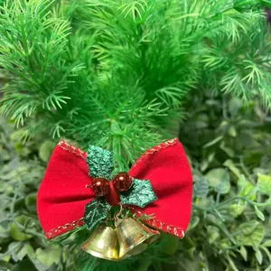 Dettaglio di un fiocco di Natale in velluto rosso con campanelli dorati e foglie di agrifoglio.
