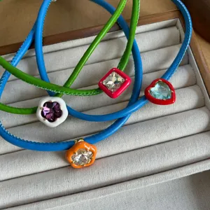 Close-up of colorful leather cord necklaces with crystal heart and flower pendants.