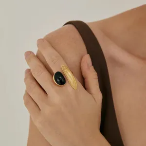 Primer plano de un anillo bañado en oro con piedras negras y ámbar en la mano de mujer.