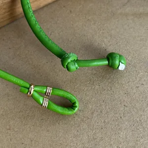 Close-up of green leather cord necklace with gold metal rings and decorative knots.