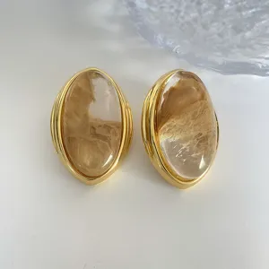 Primer plano de elegantes pendientes ovalados chapados en oro con cristales de té.
