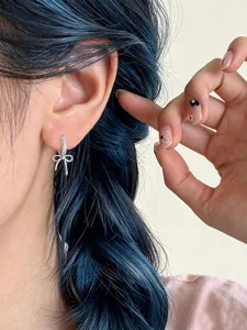 Close-up detail of silver zircon bow earrings worn on ear with blue hair background