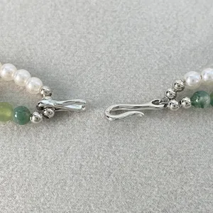 Dettaglio della chiusura a gancio a S in argento di una collana a due fili con perle e pietre.