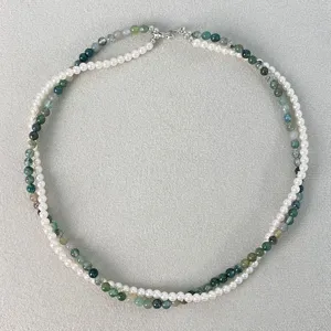 Collana a doppio strato con perle bianche e perle di agata muschiata verde su sfondo materico.