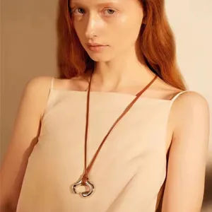 Primo piano di una collana con ciondolo in argento astratto minimalista e cordino marrone