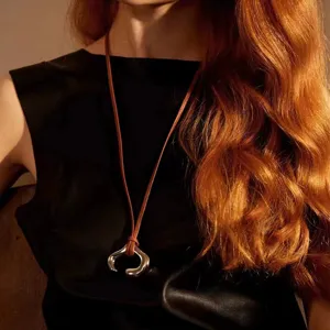 Dettaglio di un ciondolo d'argento astratto su una lunga collana in corda di cuoio.