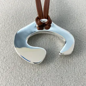 Primo piano di un pendente astratto argentato su una collana con cordino in pelle.