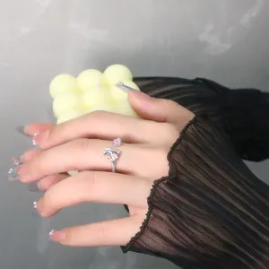 Gros plan d'une bague chat et fleur de cerisier rose sur une main avec manche noire.