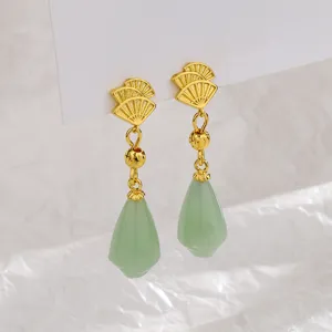 Close-up of elegant gold fan-shaped earrings with light green jade pendants