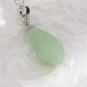 Macro detail of a light green waterdrop-shaped carved jade pendant with silver clasp.
