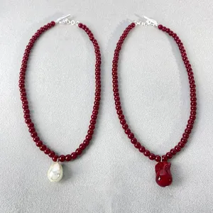 Primer plano de collares de cuentas rojas con perla blanca y colgante de corazón.