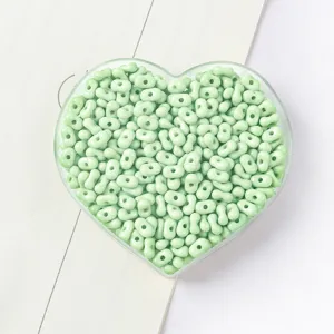 Close-up of mint green peanut-shaped beads for DIY jewelry making in a heart tray