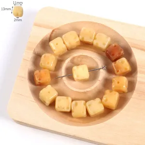 Close-up of yellow cheese dice shaped loose beads arranged on a wooden tray for DIY crafts.