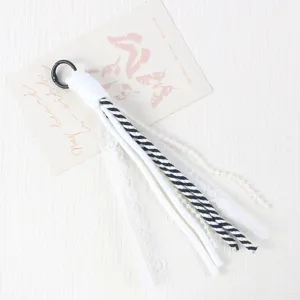 Detailed shot of DIY phone charm strap with white lace, black striped cord, and pearl beads.