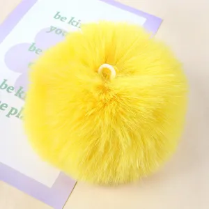 Close-up detail of a bright yellow fluffy faux fur pom pom with hanging loop, soft DIY decor.