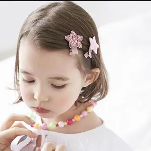 Gros plan d'une fillette portant des barrettes étoiles roses et un collier de perles coloré.