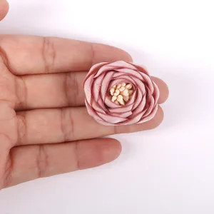 Gros plan d'une rose en tissu 3D vieux rose tenue dans une paume pour montrer l'échelle