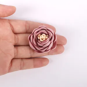 Gros plan d'une rose en tissu 3D rose poudré tenue dans une main pour montrer l'échelle