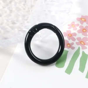 Detalle de anillo de resorte de metal negro, mosquetón abierto para joyería y bolsos.