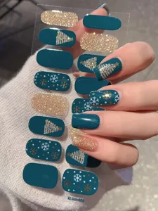 Detailaufnahme von petrolfarbenen Weihnachts-Nagelstickern mit goldenen Bäumen.
