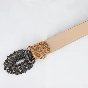 Detail view of a vintage hollowed-out metal buckle on a beige textured leather belt for jeans.