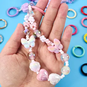 Detalle de un amuleto de cuentas pastel con mariposas y corazones sostenido en mano.