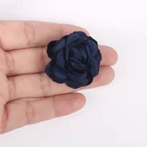 Detail view of a navy blue burnt-edge fabric rose held in a hand for scale