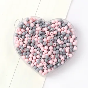 Gros plan de perles rondes en acrylique roses et grises pour bijoux DIY dans un plateau cœur