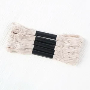Macro detail of cream-colored six-strand polyester embroidery thread bundles on white fabric