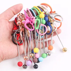 Mano sosteniendo varios llaveros de metal con cuentas de colores para decorar bolsos creativos