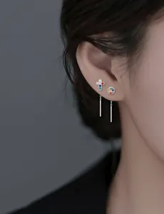 Vue détaillée de boucles d'oreilles pendantes avec croix et zircon coloré sur l'oreille