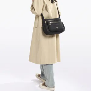 Detail of a black multi-compartment crossbody bag worn by a model in a trench coat