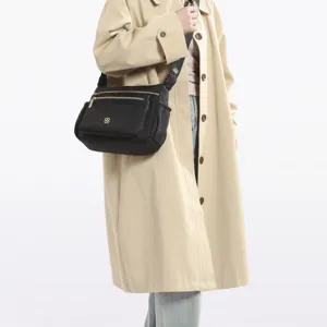 Black multi-compartment crossbody bag shown on a model wearing a stylish beige trench coat.