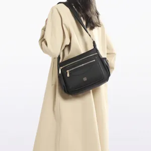 Detailed view of black multi-compartment shoulder bag worn with tan coat
