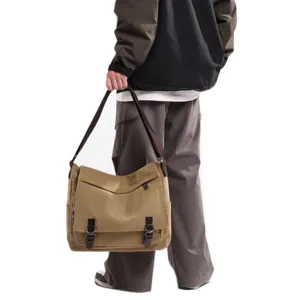 Side view of man carrying a large khaki canvas messenger bag with vintage flap closure