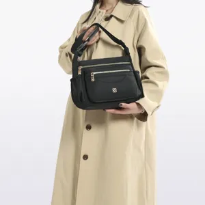 Model carrying black multi-compartment nylon shoulder bag with shiny gold zippers.