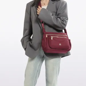 Close-up of a burgundy nylon crossbody bag with multiple functional zipper pockets.