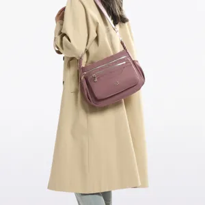 Close-up of mauve multi-compartment crossbody bag worn with a beige trench coat