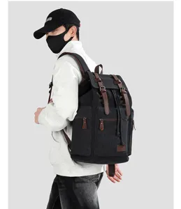 Vintage black canvas travel backpack with brown straps shown on a model's back side.