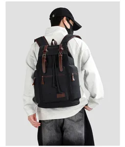 Back view of a large black canvas backpack with leather straps on a male model.