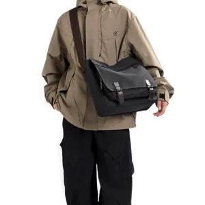Model wearing a large black canvas messenger bag for men featuring brown straps