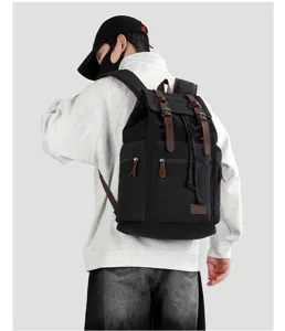 Large black canvas travel backpack with brown leather straps worn by model