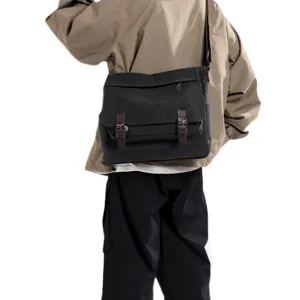 Back view of a black canvas messenger bag for men with brown leather strap details