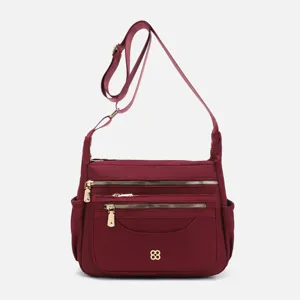 Detail of wine red multi-compartment nylon crossbody bag with gold zippers.
